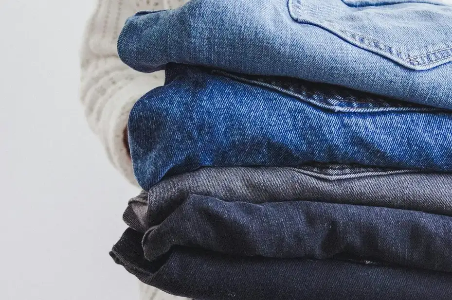 Stack of folded denim jeans in several washes held in both arms